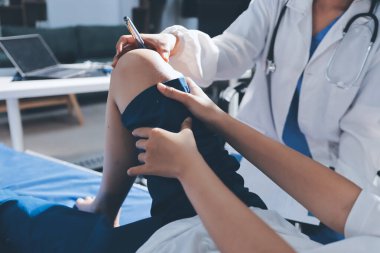 Kadın doktor elleri, erkek bir hastanın bacağını ve dizini uzatarak fizik tedavi uyguluyor.