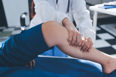 Kadın doktor elleri, erkek bir hastanın bacağını ve dizini uzatarak fizik tedavi uyguluyor.