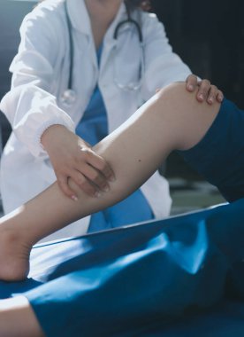Kadın doktor elleri, erkek bir hastanın bacağını ve dizini uzatarak fizik tedavi uyguluyor.