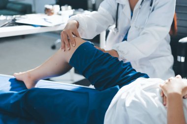 Kadın doktor elleri, erkek bir hastanın bacağını ve dizini uzatarak fizik tedavi uyguluyor.