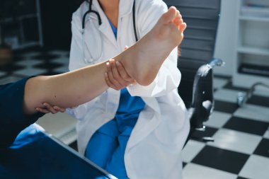 Kadın doktor elleri, erkek bir hastanın bacağını ve dizini uzatarak fizik tedavi uyguluyor.