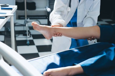 Kadın doktor elleri, erkek bir hastanın bacağını ve dizini uzatarak fizik tedavi uyguluyor.