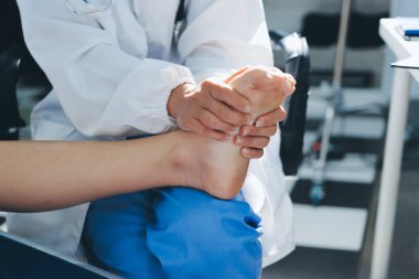 Kadın doktor elleri, erkek bir hastanın bacağını ve dizini uzatarak fizik tedavi uyguluyor.