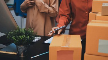 Küçük işletmeler kurma portresi KOBİ sahipleri ve iki Asyalı kadın online siparişleri kontrol ediyor. Ev işlerinde çalışan kutucuklarla çalışan ürünleri satıyorlar.