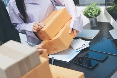 Küçük işletmeler kurma portresi KOBİ sahipleri ve iki Asyalı kadın online siparişleri kontrol ediyor. Ev işlerinde çalışan kutucuklarla çalışan ürünleri satıyorlar.