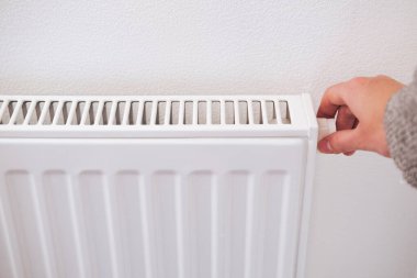 Merkezi ısıtma radyatörünün termostatını kapatan el. Enerji tasarrufu, soğuk kış mevsimi, düşük enerji tüketimi ve ekonomi teması.