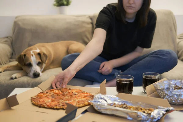 自宅で配達されたピザを食べる 女性はピザのスライスをつかむ ソファの上に犬を見て 食べ物に焦点を当てる ストックフォト