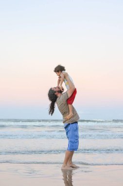 Bir baba, güzel bir günbatımında oğlunu sahilde saf mutlulukla kucağına alır. Dalgalar, yumuşak günbatımının gökyüzünü pastel renklerle renklendirmesi gibi nazikçe kumu öpüyor. Aşkları ve neşeleri çok açık..