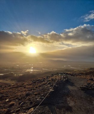  the golden hour sunlight spilling over a rocky plain stretching to the horizon and a bright sun piercing the clouds with its rays clipart