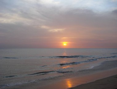 Sakin bir sahilde sakin bir günbatımının sakin bir sahnesi. Güneş ufukta batıyor, gökyüzünde bir dizi sıcak renk bırakıyor, yumuşak dalgalar kumlu kıyıya vuruyor..