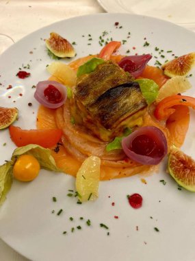 Çok güzel hazırlanmış somon balığı dilimleri, ızgara balık, renkli incir, turşu dilimleri, beyaz bir tabakta soğan ve böğürtlen turşusu, otlarla süslenmiş..