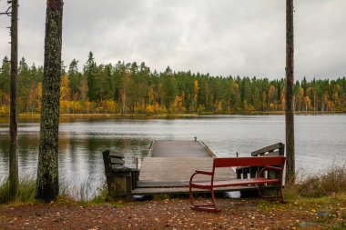 Huzurlu göle bakan kırmızı bankları olan sakin ahşap rıhtım, altın sonbahar ormanı ve bulutlu gökyüzü altında daima yeşil ağaçlarla çevrili, doğada sakin bir geri çekilme yaratıyor. Finlandiya, Avrupa 'da yakalandı.