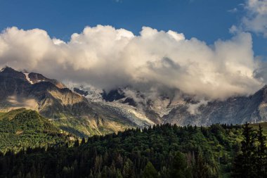 08-24-2021 - Gökyüzü bulutlu Alpler 'in tepelerinin panorama manzarası, Fransa' daki yeşil orman akşam güneşinde Mont Blanc 'ın tepesine normal bir yol