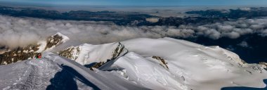 08-27-2021 - Mont Blanc buzulunun tepesinden aşağı inen tırmanışçıların panorama manzarası, sabah güneş ışınları, açık mavi gökyüzü ve vadide alçak bulutlar