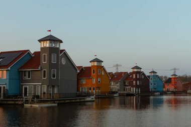 Huzurlu bir kanalı çevreleyen kule benzeri yapılara sahip canlı modern evler, akşam ışığının sıcak tonlarını yansıtıyor. Çağdaş Hollanda liman mimarisinin çarpıcı bir örneği. Groningen, Hollanda, Avrupa 'da yakalandı.