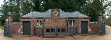 Süslü bir saat ve sağlam demir kapıların yer aldığı güzel korunmuş tarihi tuğla bir yapı, ünlü Hoge Veluwe Ulusal Parkı 'nın girişini işaret ediyor, kültürel mirası doğal güzellikle harmanlıyor. Hoge Veluwe Ulusal Parkı 'nda yakalandı.