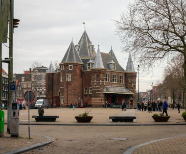 10-03-2024 - Amsterdam, Hollanda - Amsterdam 'ın mimari cazibesini yansıtan insanlar, banklar, ağaçlar ve şehir manzarası ile çevrili şehir meydanında bulunan tarihi kale benzeri kuleler. Amsterdam, Netherlan 'da yakalandı.