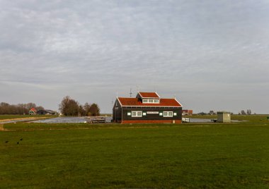 10-03-2024-Hollanda - çarpıcı kırmızı çatılı geleneksel Hollanda kır evi, yemyeşil alanlar ve durgun su yansımaları arasına yerleşmiş, pitoresk bir kırsal ortam yaratıyor. Hollanda, Avrupa 'da Yakalandı