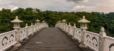 Jeju Adası 'nda bulutlu bir gökyüzü altında yemyeşil bir alana uzanan karmaşık beyaz parmaklıklar ve taş fenerler ile zarif kemerli taş köprü huzurlu bir manzara yaratıyor. Jeju, Güney Kore ve Asya 'da yakalandı.