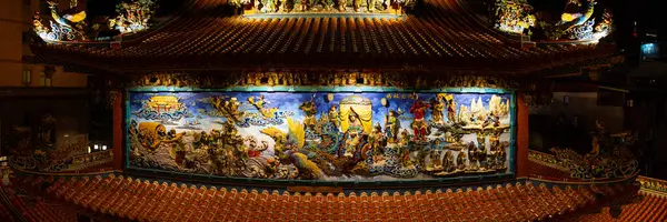Göksel varlıkları, antik tanrıları ve efsanevi hikayeleri tasvir eden büyük mitolojik duvar resmi geleneksel tapınak cephesinde canlı renklerle ve gece aydınlatılmış süslü detaylarla karmaşık bir şekilde tasarlanmıştır. Tayvan, Asya 'da yakalanmış..