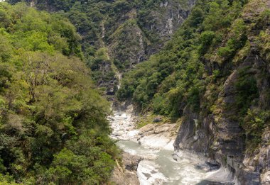 Dik vadide hızlı nehir esiyor, yoğun yeşil bitki örtüsü ve dramatik uçurumlarla çevrili pürüzsüz mermer kayalar oyuyor, işlenmemiş manzaranın ham güzelliğini sergiliyor. Taroko Milli Parkı, Tayvan, Asya 'da yakalandı.