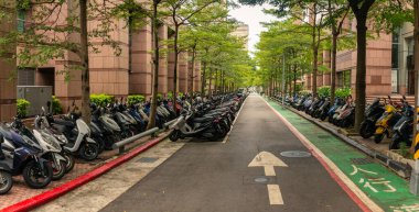 14-08-2023 - Taipei, Tayvan: Uzun sıra park halindeki scooterlar ağaç gölgeli şehir geçidi boyunca düzenli olarak düzenlenerek, modern altyapıya sahip hareketli şehir ortamında iki tekerli taşımaya yüksek güvenilirliği yansıtıyor. Tayvan, Asya 'da yakalanmış..