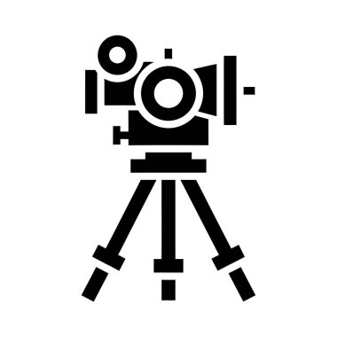 Siyah bir teodolit, bir inceleme aracı, bir tripodun üzerinde duruyor. Tasarım basit ve geometrik, dairesel ve dikdörtgen şekilli..