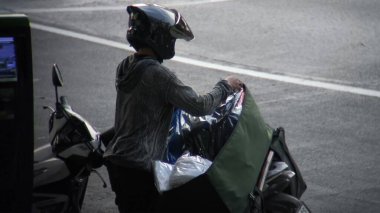 Motosikletli bir teslimatçı. Paketlenmiş mallarla dolu. Şehir caddesinde geziniyor. Sahne, taşıma işinin pratik ve verimli doğasını gözler önüne sererek bir şehir koşuşturması anı yakalıyor..