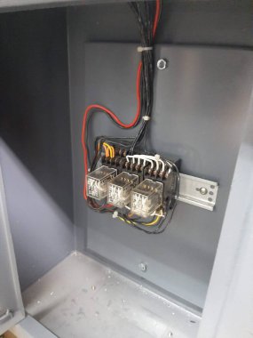 Üç elektrik rölesi gri metal bir kutunun içine yerleştirilmiş ve çeşitli kablolar birbirine bağlanmış. Kablolar çok karmaşık..
