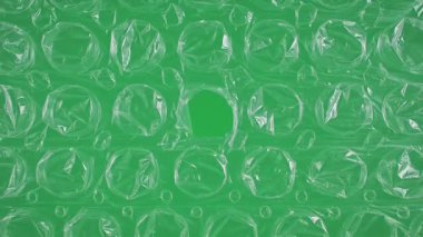 Kabarcık ambalajı, yeşil arka planda bir delikle yakın plan. Plastiğin dokusu görülebilir..