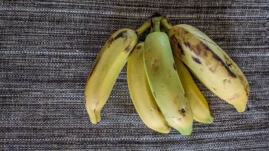 Yukarıdan bir demet muz görünüyor, masa örtüsü üzerinde. 