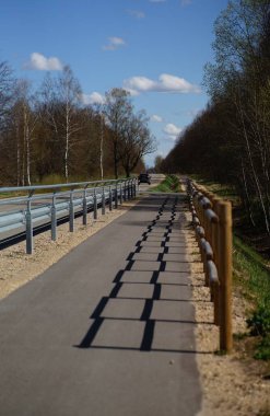 Sağlam tırabzanlarla kaplı bir köy yolu uzak bir arabaya doğru uzanan entrika dolu gölgeler bırakır. Bu huzurlu, açık yol boyunca yolculuk ve macera hissi uyandırır..