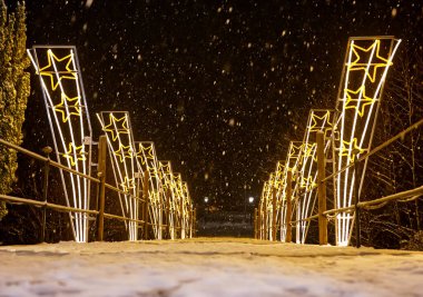 Geceleri yıldız şeklindeki ışıklarla aydınlatılmış karla kaplı bir köprü..