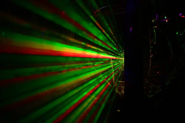 Karanlık bir ortamda yeşil ve kırmızı lazer ışınlarının soyut görüntüsü geleceksel ve dinamik bir görsel etki yaratıyor..