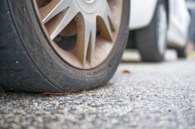 Pürüzlü asfalt bir zeminde, arka planda başka bir araçla patlak bir araba lastiğinin yakın çekimi..