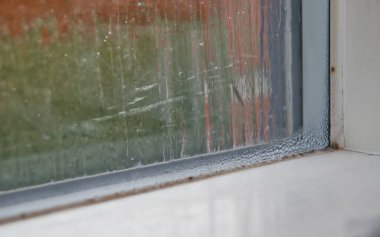 Yağmur damlaları ve yoğunlaşması olan pencerenin yakın plan görüntüsü, dışarıda bulanık bir görünüm gösterir.