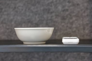 Basit bir beyaz seramik kase, küçük beyaz bir elektronik aletin yanına koyulmuş, minimalist bir estetik yaratıyor..