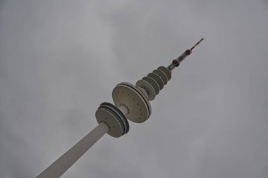 Belirgin bir tasarımı olan, bulutlu bir gökyüzüne karşı yükselen uzun bir telekomünikasyon kulesi. Kulede birden fazla dairesel platform ve tepesinde kırmızı-beyaz bir anten bulunur..