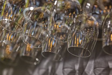 Gözlüklerin yansımalarını ve şeffaflığını gösteren, asılmış camların yakın çekim görüntüsü. Arka planda bulanık ışıklar var, sıcak bir ortam yaratıyor..