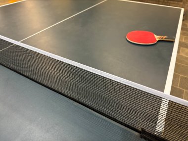 Yüzeyinde kırmızı bir kürek bulunan masa tenisi masasının yakın çekim görüntüsü. Ağ ön planda, sporun düzenini vurguluyor..