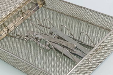 İçinde kıskaçlar ve kıskaçlar da dahil olmak üzere çeşitli cerrahi aletlerin bulunduğu metal bir tepsinin yakından görüntüsü düzgünce düzenlenmiş. Tepsi desenli bir yüzeye sahiptir ve paslanmaz çelikten yapılmıştır..