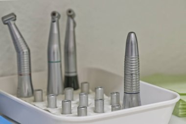 Diş telleri ve eklentiler de dahil olmak üzere çeşitli diş aletlerini içeren bir tepsi, beyaz bir bez üzerine güzelce yerleştirilmiş. Arkaplan yumuşak bulanık, araçları vurguluyor.