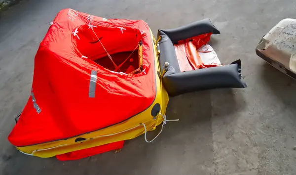 Parlak kırmızı bir gölgelik ve sarı tabanlı, kısmen gri bir yüzeye yerleştirilmiş şişirilebilir bir cankurtaran salı. Sal denizdeki acil durumlar için tasarlandı..