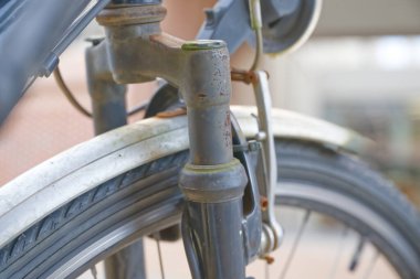 Bisikletin ön çatal ve tekerleğinin yakın çekimi, paslanmış ve aşınmış metal parçaları gösteriyor, bulanık bir arka planı var..