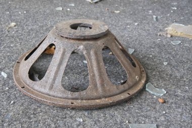 Konik şekilli paslı, dairesel metal bir nesne. Kırık cam ve molozlarla dolu kirli bir yüzeye yayılmış..