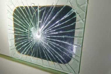 Merkezden yayılan yıldız patlaması desenli parçalanmış cam panelin yakın çekim görüntüsü. Cam çatlamış ve kırılmış. Arkasında karanlık bir zemin var..