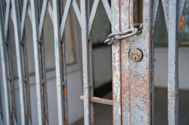 Paslı, zincirli ve asma kilitli metal bir kapının yakın çekim görüntüsü. Kapı bir zikzak deseni içeriyor ve yıpranma ve yıpranma izleri gösteriyor, yaşını ve ihmalini gösteriyor..