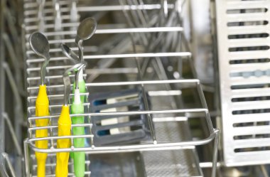 Renkli kaşıklar ve metal rendesi de dahil olmak üzere çeşitli çatal bıçakların yer aldığı bir bulaşık rafının yakın çekim görüntüsü. Çatal bıçaklar düzgün düzenlenmiş, metalik arka plana karşı sarı, yeşil ve mavi renklerin karışımını sergiliyorlar..