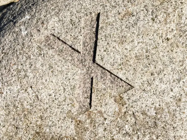 Yüzeyine çapraz bir sembol kazınmış oyulmuş bir taşın yakın çekim görüntüsü. Taşın dokusu pürüzsüz ve doğal görünür tanecikleri ve renkleri var..