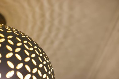 Karmaşık kesik desenli dekoratif bir lambanın yakın plan görüntüsü, desenli bir tavana yumuşak bir ışık yansıtıyor..